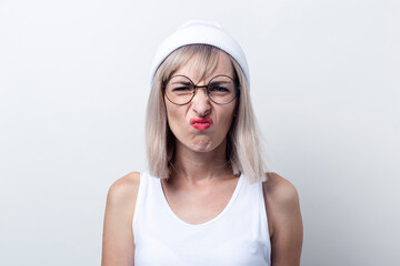 Blond young woman twisted with glasses, a white hat on a light background