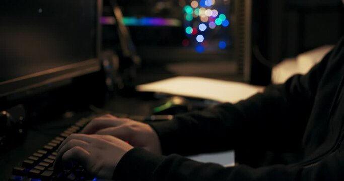 Close-up of boy's hands typing on keyboard. Hacker has new task, which he successfully completed. The guy smiles, rubs hands, takes cup of coffee and takes sip. The man has beard and cap on head.