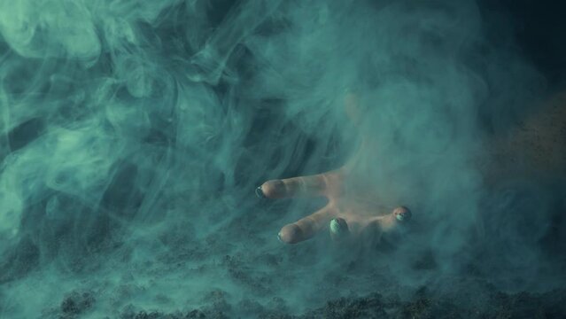 A terrible hand with claws emerges from the fumes of smoke over the graveyard ground.