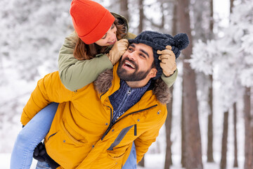 Boyfriend piggybacking girlfriend in the snow while on winter vacation in the mountains