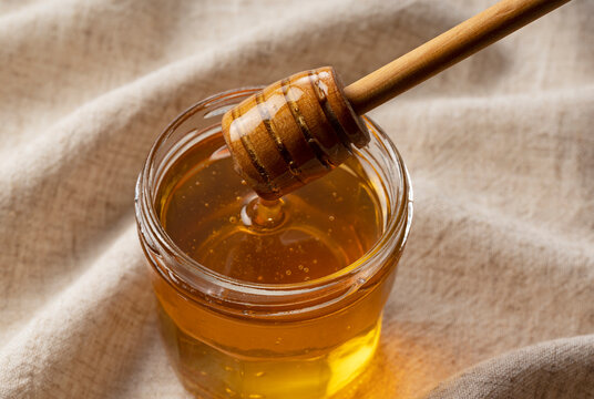Honey in glass container and wooden honey dipper on cloth background.