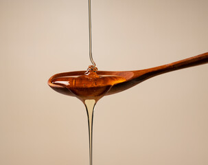 Honey and wooden spoon on beige background.