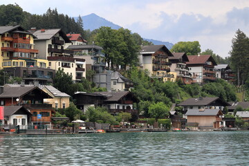 Fototapeta na wymiar View from Lake Wolfgangsee to the buildings on the shore. Tourist and recreation area in the Austrian Alps. A lake, a wharf, houses on a hill by the coast.