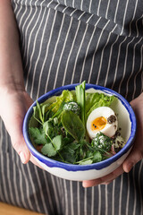 female hands holding bowl of fresh green salad with egg half
