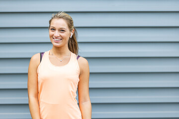 Portrait of beautiful fitness woman smiling and looking at camera isolated on grey background. Laughing mid woman in sportswear wearing wireless headphones and relaxing after training at gym. 