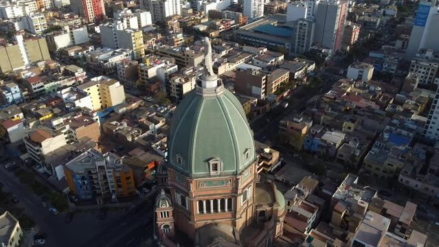 Drone 4k video of a church. Drone orbits around the dome with statue of the virgin mary on top. Many buildings behind and around the church. Located in Lima, Peru.
