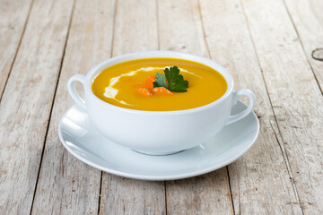 Carrot soup with cream and parsley on rustic wooden table