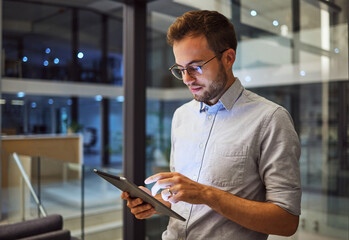 Man in office, working on tablet at night in the office and testing campaign strategy for marketing...