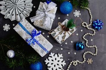 Layout of New Year's decor in white, blue and silver colors and gift boxes on a dark gray background. View from above