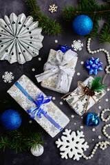 vertical composition. New Year's decor, snowflakes, balls and Christmas tree decorations in white, blue and silver colors and gift boxes on a dark gray background. View from above.