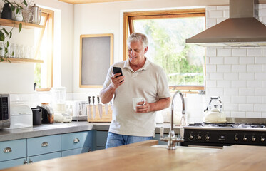Senior man, morning coffee and phone looking happy while reading text message, online news or browsing internet in kitchen at home. Male using messenger or social media mobile app in Australia house