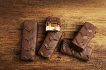 Chocolate bars with caramel, nuts and nougat on wooden table, flat lay