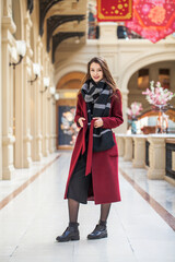 Fototapeta premium Portrait of a young brunette girl in a crimson red autumn coat