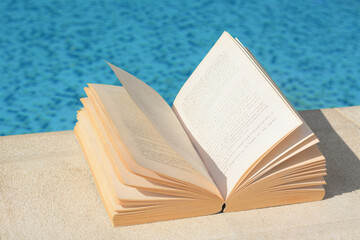Open book on swimming pool edge during sunny day