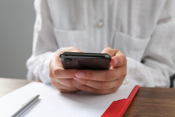 Woman using smartphone at wooden table in office, closeup