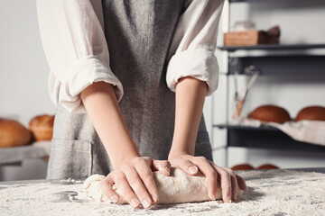 Woman kneading dough at table in kitchen, closeup