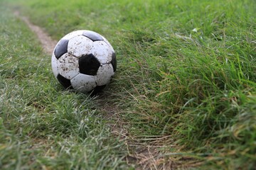 Dirty soccer ball on green grass outdoors, space for text