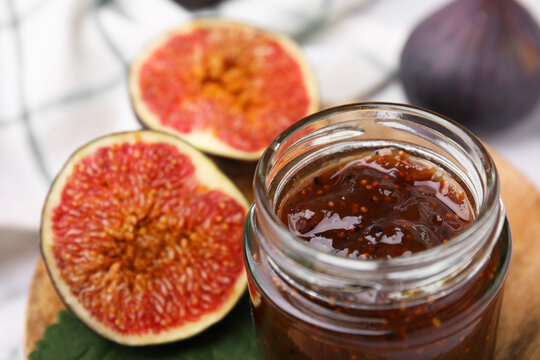 Tasty sweet fig jam in jar and fruits on table, closeup
