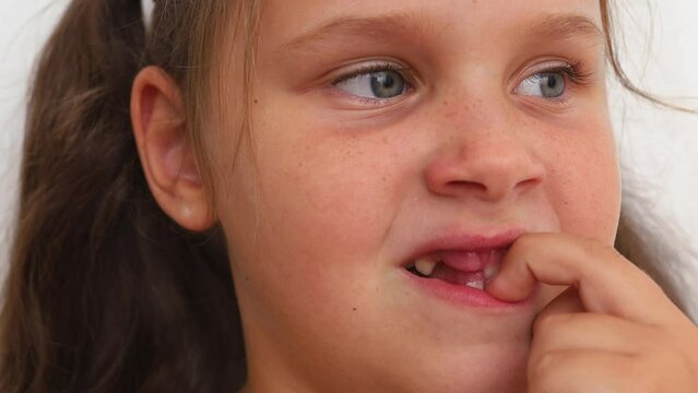 Thoughtful, stressed, emotional nervous blond little girl with blue eyes picking teeth in toothless mouth with fingers while look away on white background. Cleaning milk baby teeth, bad habits