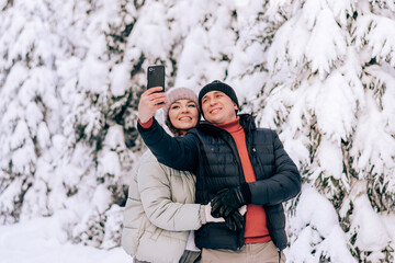 Young couple in love take a selfie on a smarfton while walking in the winter forest.Winter activities,active lifestyle,Valentine's day,tenderness and love.