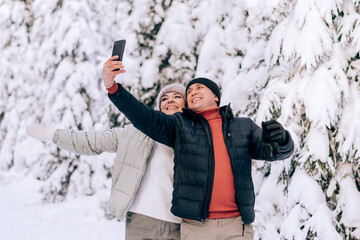 Young couple in love take a selfie on a smarfton while walking in the winter forest.Winter activities,active lifestyle,Valentine's day,tenderness and love.