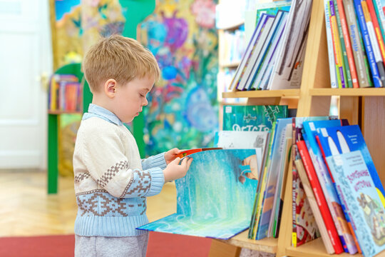 A little boy in the library is leafing through a children's picture book with interest. The child is drawn to knowledge. The concept of early development
