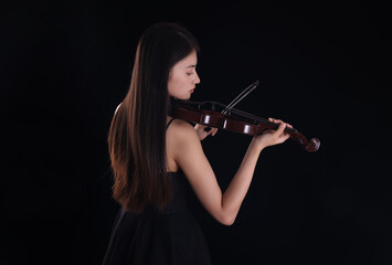 Fototapeta premium A young woman playing a violin on a black background
