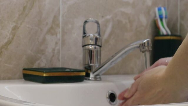 Wash hands with soap. The girl turns on the water tap, takes the soap and lathers her hands, washes her fingers thoroughly and rinses everything off with water. Video HD
