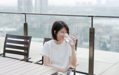 Fototapeta premium Relaxed woman sitting in chair on balcony and holding a glass of water 