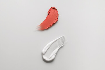 Lipstick and skin care cream smear swatch set on a white background. Makeup cream brushstroke texture. Red-orange lipstick swatch product close up.