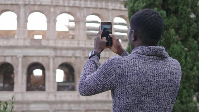 Young african american man holding smartphone taking pictures at the Collosseum