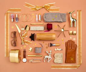 Christmas objects gifts and decorations laid out in the shape of a gift box with golden ribbon and bow. Accessories, makeup and cosmetics as a presents ideas. Gifts guide for her. Overhead view.
