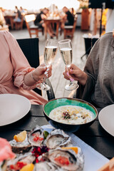Two Women friends eating fresh oysters and drinking chilled prosecco wine on the summer sunset in restaurant. Seafood delicacies