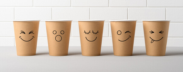 Row of paper cups with funny emotional faces on white background. Eco friendly take away cups for coffee. Banner.