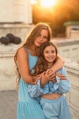 Portrait of mother and daughter in blue dresses with flowing long hair against the backdrop of...