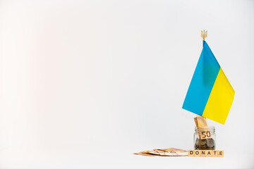 Donation for Ukraine concept. Donation jar with coins, euro and Ukrainian flag and wooden letters