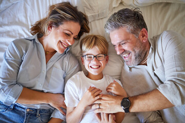 Family, tickling and child lying on bed with his happy mom and dad laughing and having fun in their bedroom at home. Portrait of boy kid with a man and woman parents to relax in their Australia house - obrazy, fototapety, plakaty