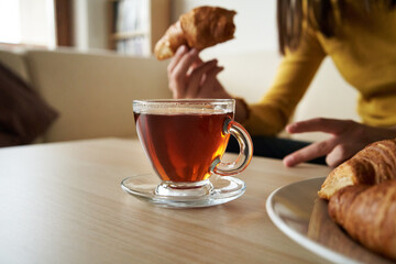 Cup of tea on a table with teenager eating croissant in the background