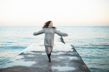Young happy woman wearing a wool sweater standing on the beach in winter enjoying the snowfall