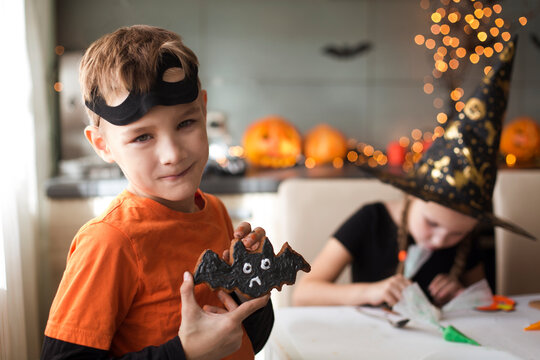 children in masquerade costumes  paint gingerbread for the halloween holiday at home in the kitchen
