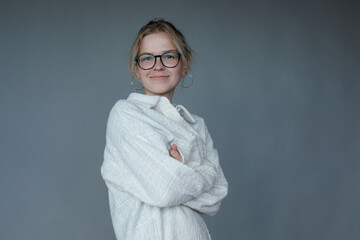 Smiling young woman in black glasses get warm by crossing arms, gray background, free copy space....