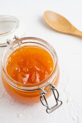 Aerial view of open glass jar with pumpkin jam on white table with wooden spoon, selective focus, white background, vertical, with copy space