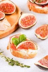 Bruschetta with raw ripe fig, cream cheese, prosciutto, walnuts and herbs on white table. Healthy quick breakfast idea. Italian cuisine. Selective focus, vertical image