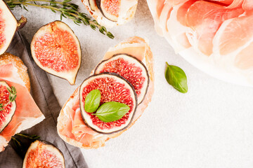 Fresh bruschetta with ripe fig, cheese, prosciutto and herbs over white concrete table background with copy space - healthy quick breakfast toast recipe. Top view, selective focus