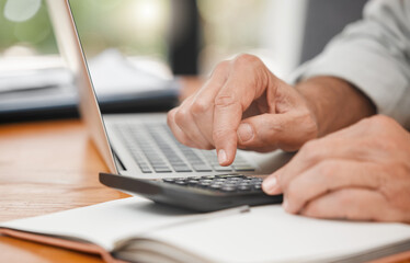Fototapeta na wymiar Calculator, laptop and hands of man calculating, accounting and home budget while doing online payments and sitting at a table at home. Closeup of a mature male accountant doing finance planning