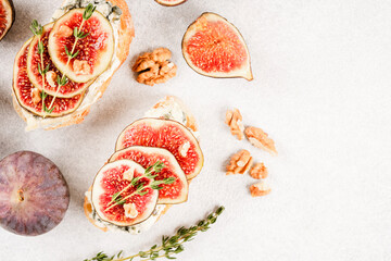 Healthy quick breakfast ideas - fresh bruschetta with ripe fig, cheese and herbs over white concrete table background. Top view, selective focus