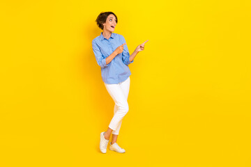Fototapeta na wymiar Full length photo of good mood excited girl dressed blue looking pointing two fingers empty space isolated yellow color background