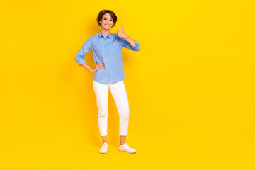 Fototapeta na wymiar Full length photo of cute confident girl dressed blue shirt showing thumb up empty space isolated yellow color background