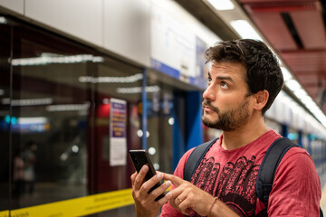 Hombre en estación de subte verificando su recorrido en tren en una aplicación de su celular - obrazy, fototapety, plakaty