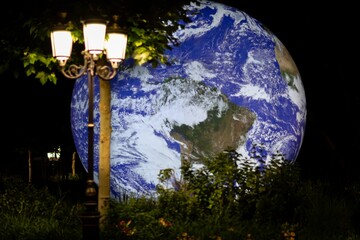 Large hologram of the planet earth at night with a street light and greenery in a park